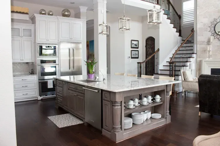 Bright white kitchen with a large island, dark wood floors, and built-in stainless steel appliances