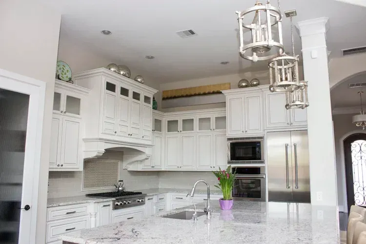 Bright white modern kitchen with marble island, stainless appliances, and hanging lantern lights
