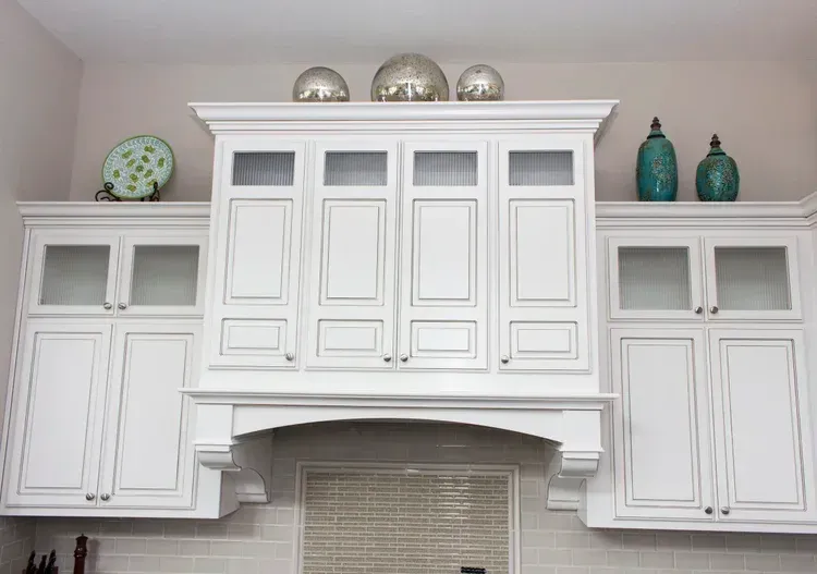 White kitchen cabinets with decorative shelves, teal vases, and silver bowls above a range hood.