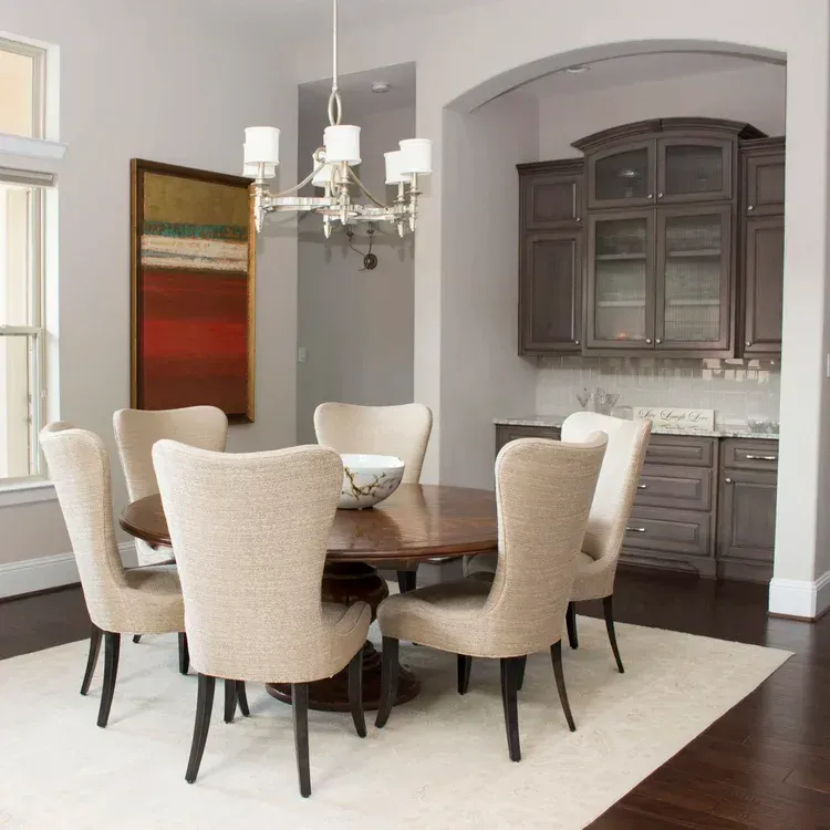 Elegant dining room with round wooden table, beige chairs, chandelier, and dark wood cabinets