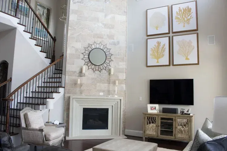 Bright living room with staircase, fireplace, round mirror, and wall art above a TV console.
