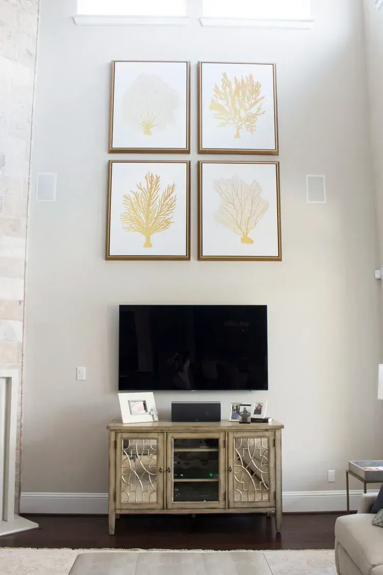 Living room wall with four gold leaf art prints above a TV console and mirror-front cabinet