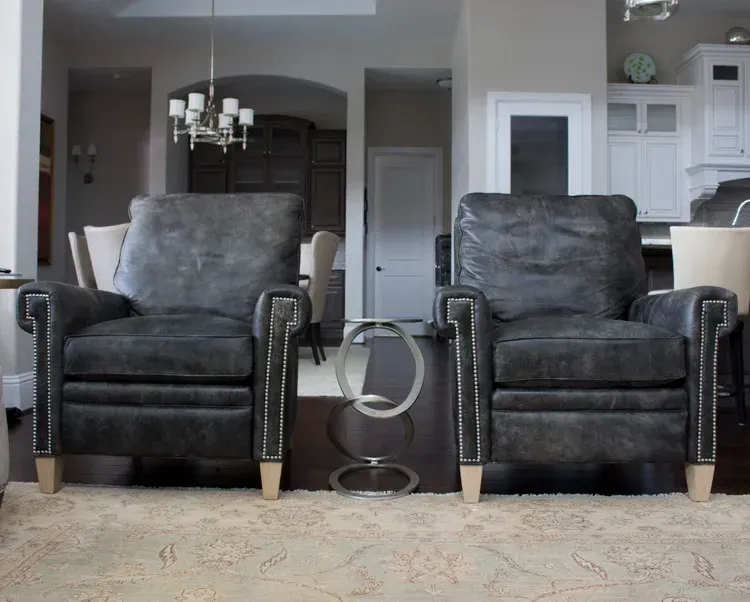 Two black leather recliners in a living room with a glass side table between them