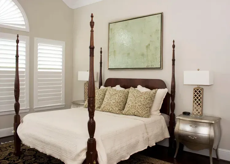 Elegant bedroom with four-poster bed, beige bedding, silver nightstand, and large wall art