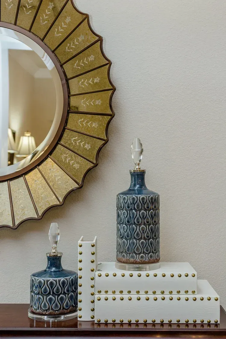 Decorative shelf with blue and white canisters and books beside a gold sunburst mirror