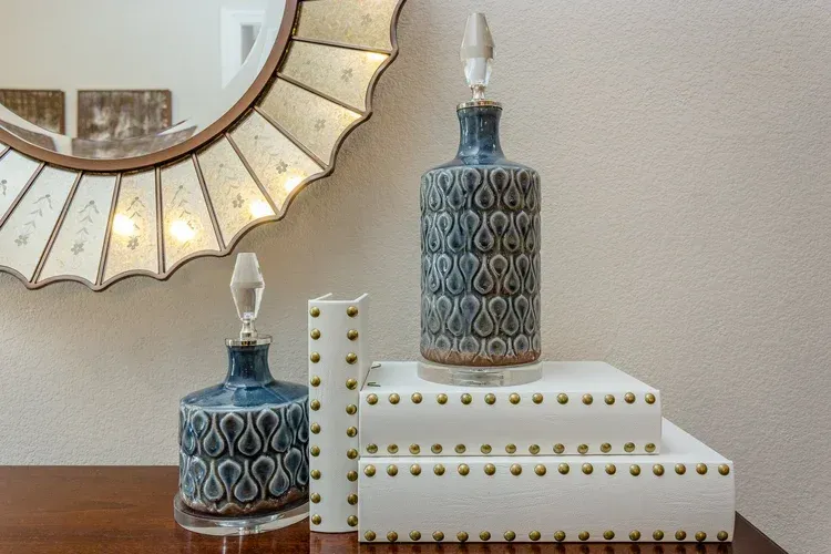 Decorative blue and white bottles on stacked white boxes beside a sunburst mirror.