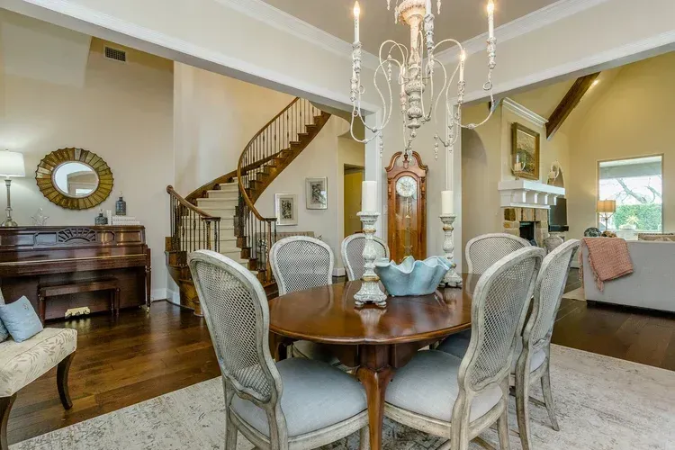 Elegant dining room with round table, chandelier, piano, and staircase in a bright open living space