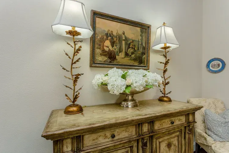 Decorative dresser with lamps, floral arrangement, and framed artwork on a white wall