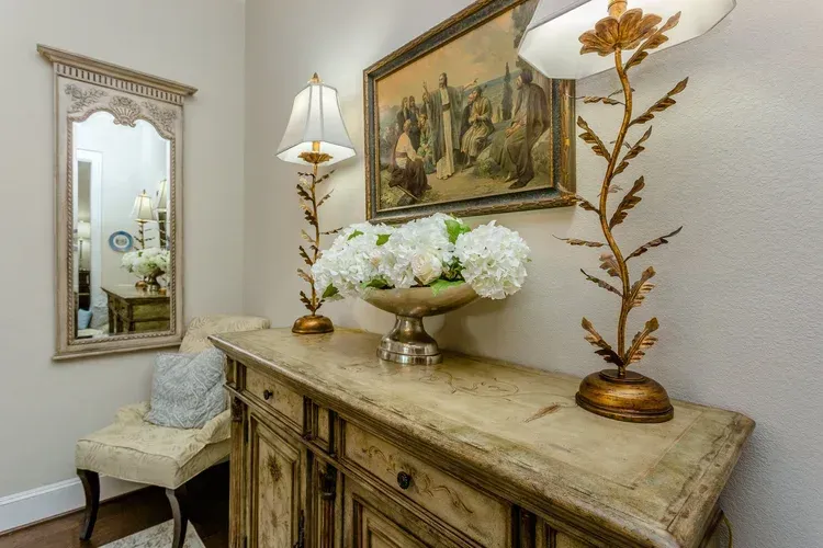Elegant hallway with ornate console table, mirror, lamp, floral arrangement, and framed painting
