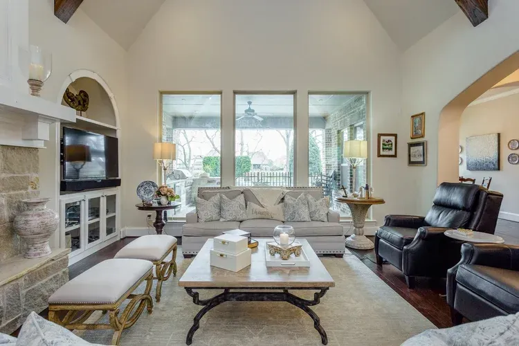 Bright living room with white sofas, leather chairs, fireplace, coffee table, and large windows