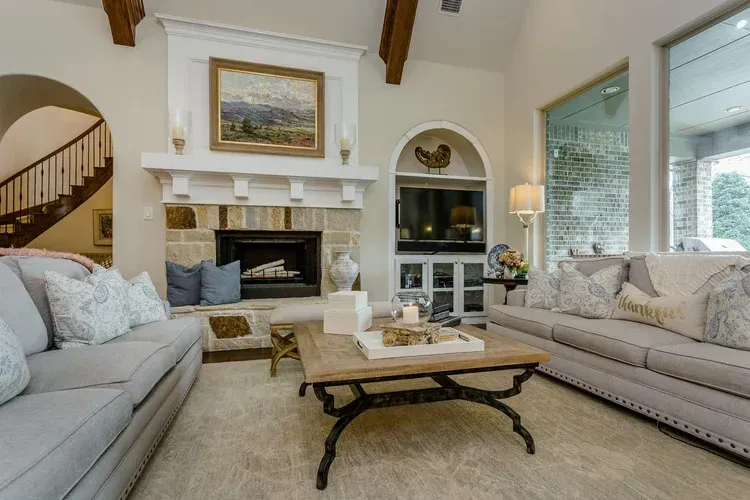 Elegant living room with fireplace, beige sofas, wood coffee table, and large windows