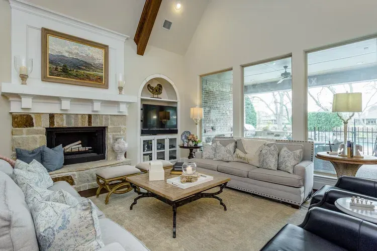 Bright living room with white fireplace, large windows, and beige sofas around a coffee table