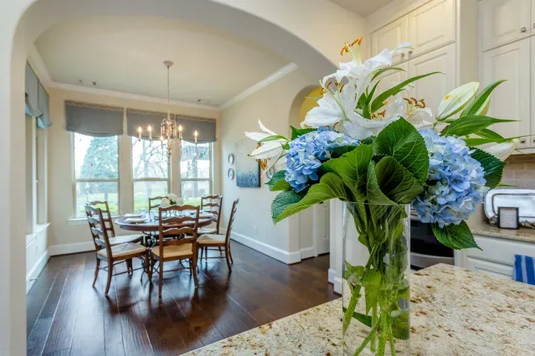 Bright kitchen with dining nook and a vase of blue-and-white flowers on a granite island.