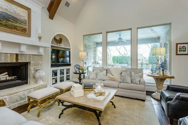 Elegant living room with stone fireplace, beige sofa, glass coffee table, and large windows overlooking trees