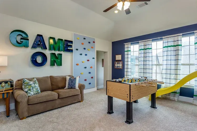 Game room with couch, foosball table, yellow slide, large windows, and “GAME ON” wall decor