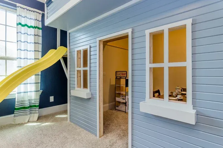 Children’s playhouse with a yellow slide, blue siding, and white-trimmed windows indoors