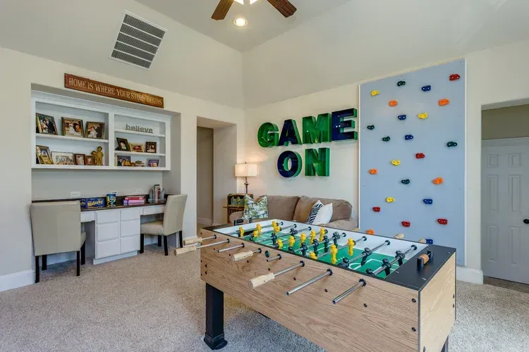 Bright game room with foosball table, wall art, desk, and colorful climbing wall panel