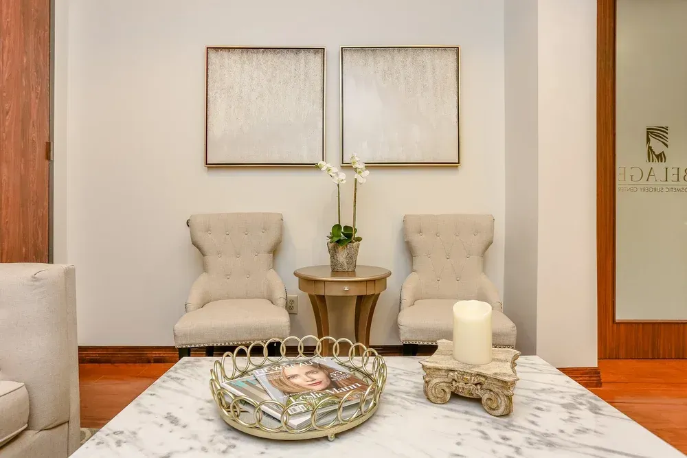 Elegant living room with two beige chairs, small table, marble coffee table, and framed wall art.