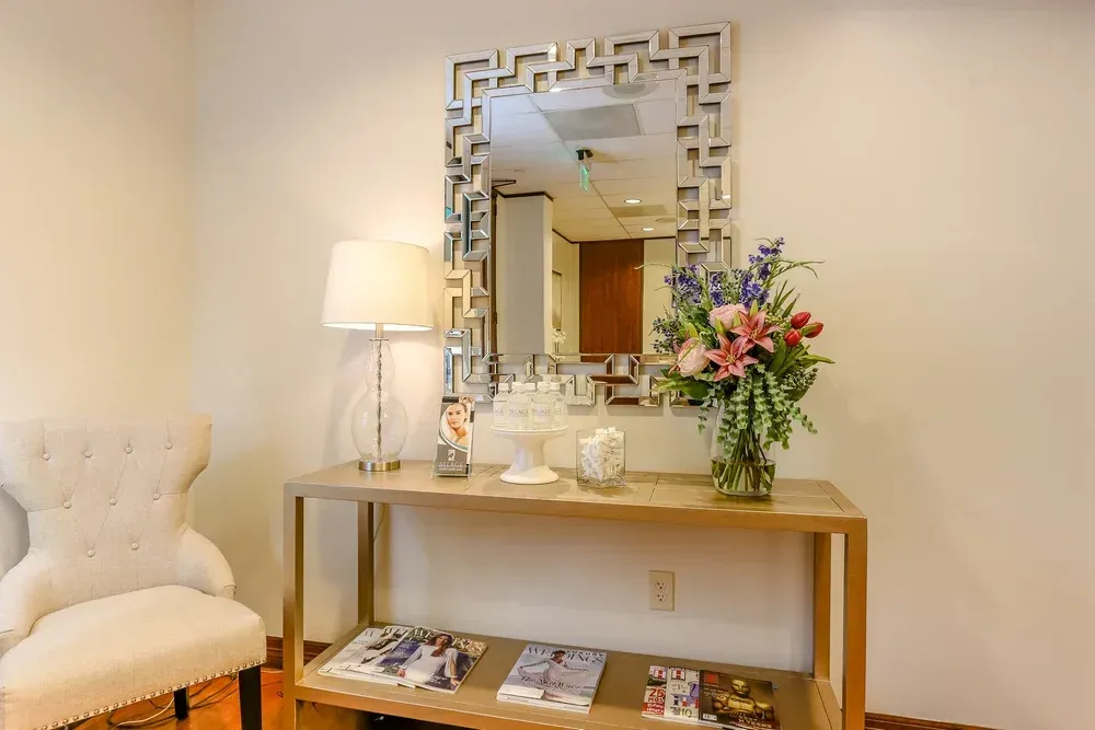 Elegant room with tufted chair, lamp, mirrored console, and pink floral arrangement