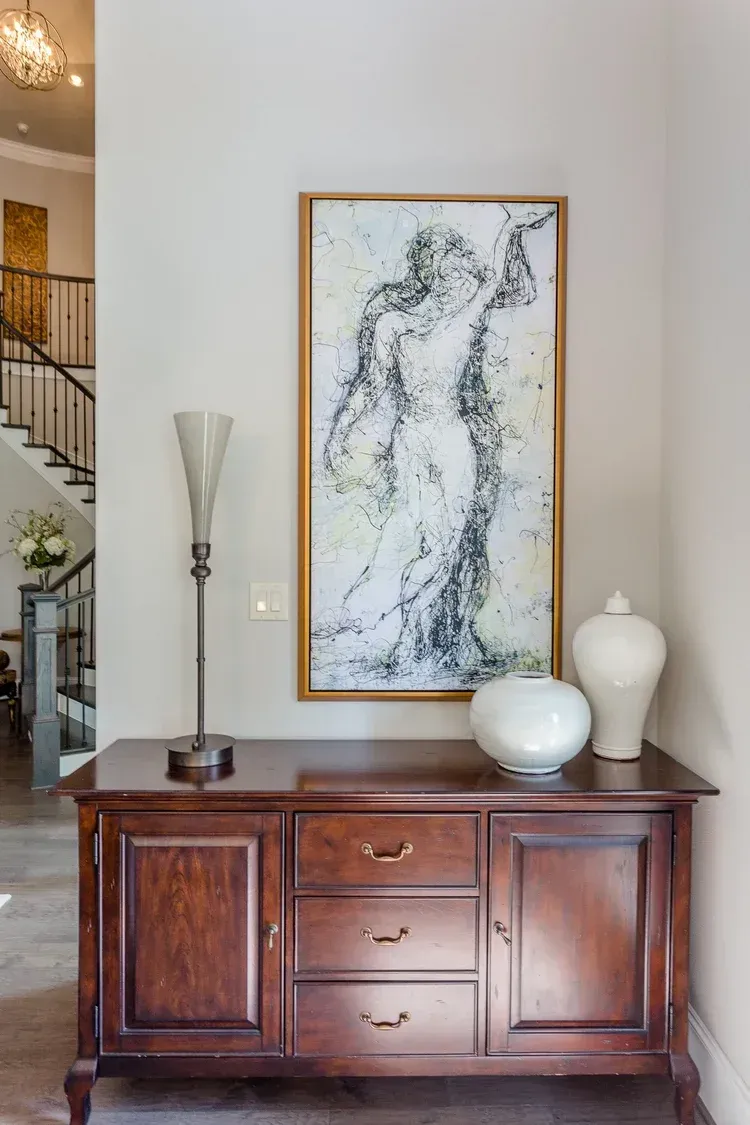 Wooden sideboard beneath abstract framed art, flanked by white vases in a bright foyer