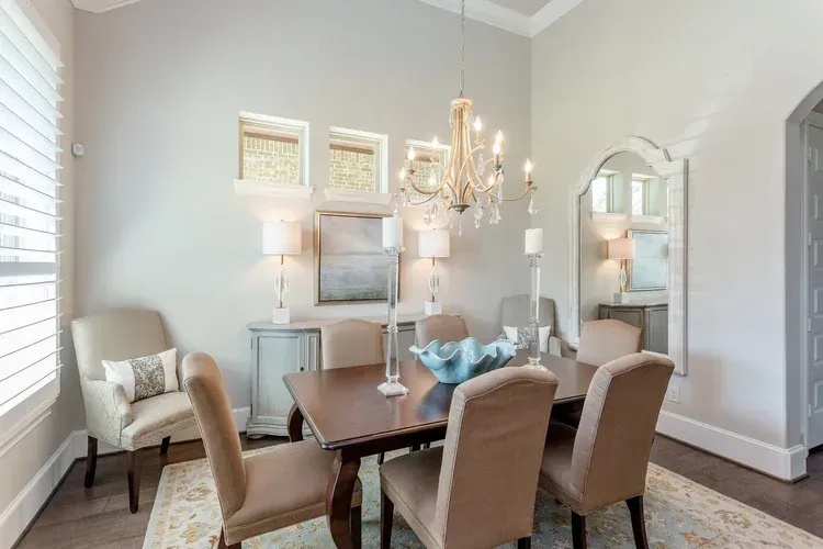 Elegant dining room with a dark wood table, beige upholstered chairs, chandelier, and gray walls