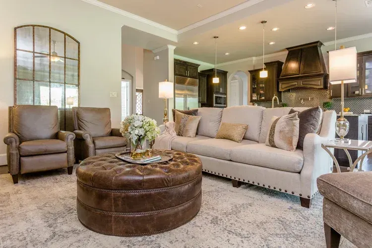 Elegant living room with beige sofa, brown ottoman, armchairs, and modern fireplace kitchen backdrop
