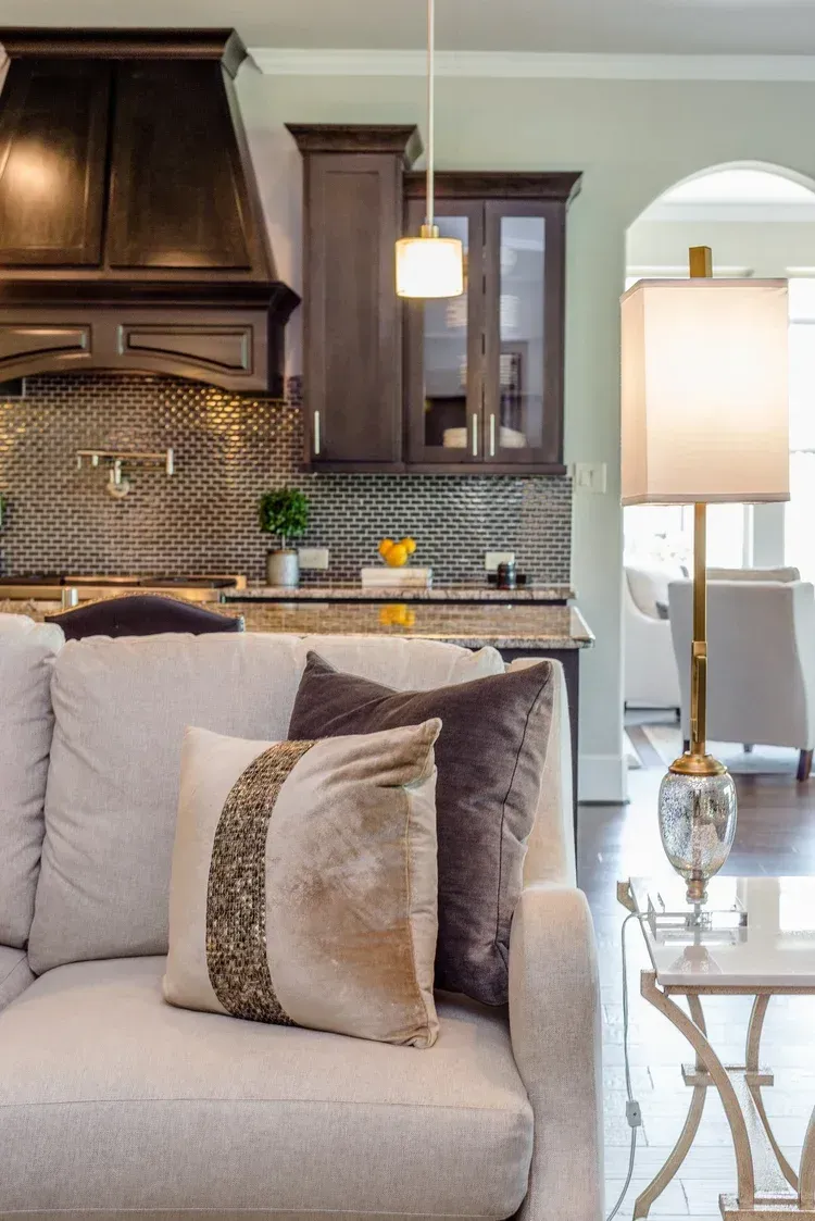 Elegant living room with beige sofa, decorative pillows, pendant light, and dark wood kitchen in the background
