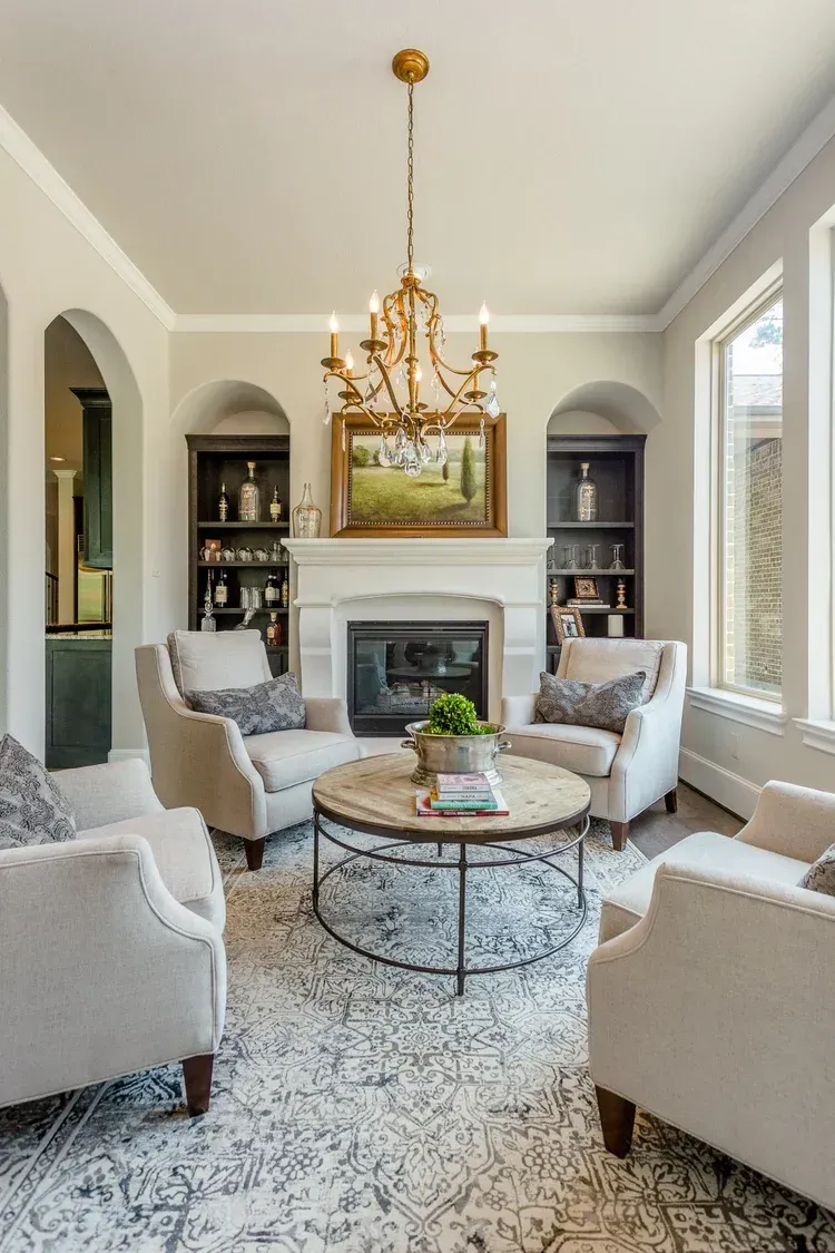 Elegant living room with a fireplace, chandelier, arched shelves, and neutral upholstered chairs