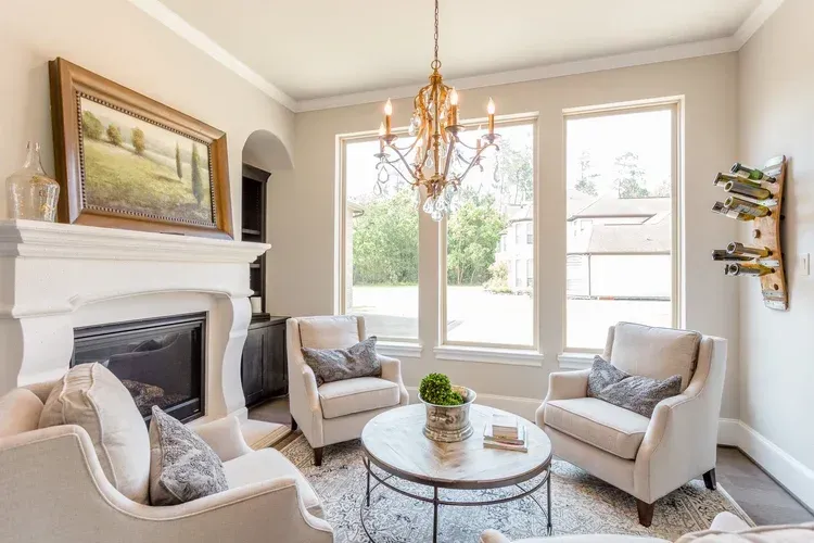 Bright living room with fireplace, four chairs, round coffee table, and large windows above a rug