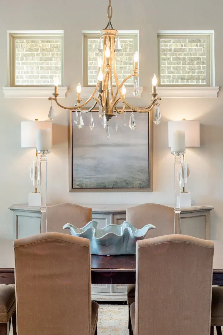 Elegant dining room with chandelier, mirrored sideboard, lamps, and two upholstered chairs