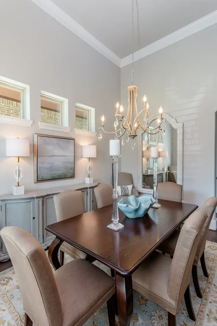 Elegant dining room with chandelier, dark table, upholstered chairs, and decorative mirror and lamps.