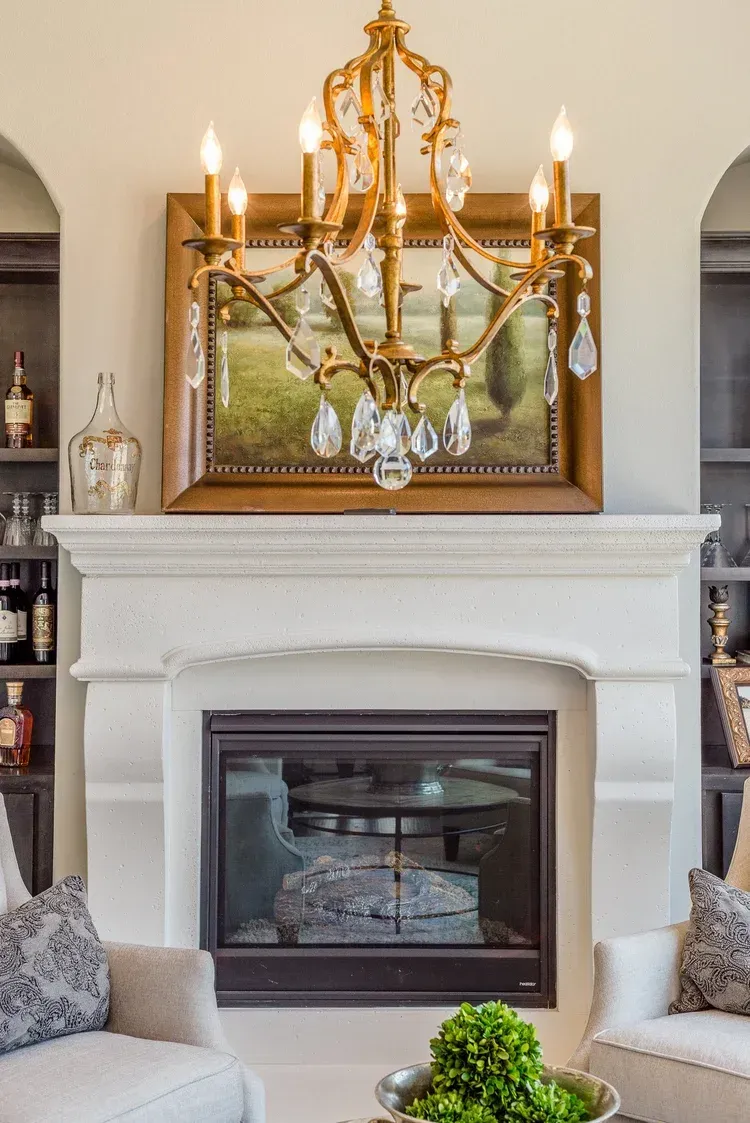 Elegant living room fireplace with ornate gold chandelier and framed artwork above the mantel