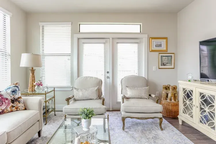 Bright living room with white chairs, sofa, glass coffee table, and French doors