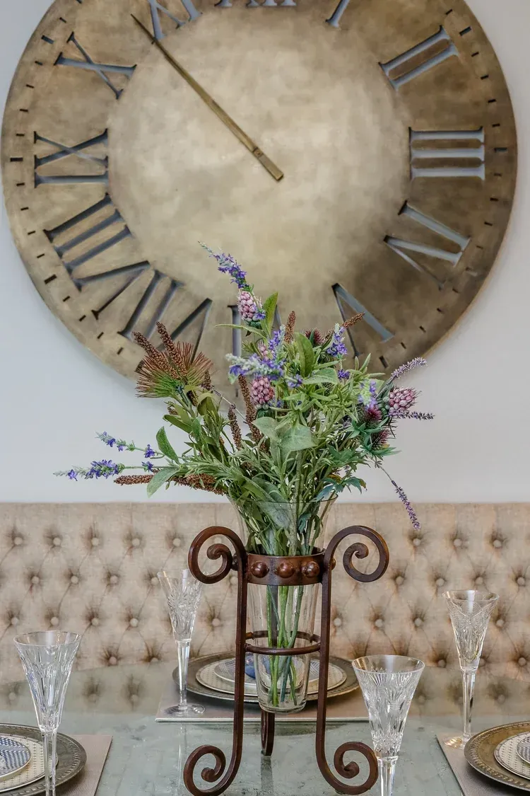 Rustic dining table with floral centerpiece before a large Roman numeral wall clock