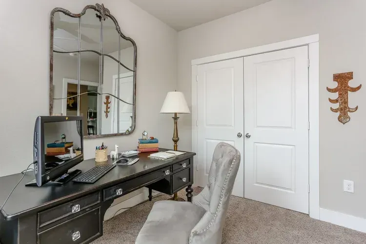 Home office with a black desk, ornate mirror, lamp, chair, and white double closet doors.