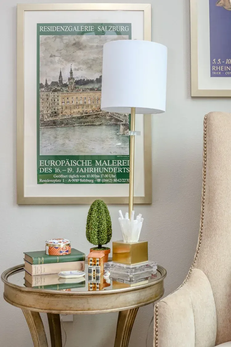 Cozy corner with a round side table, lamp, books, small cactus, and framed wall art.