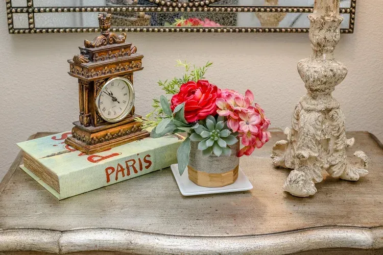 Decorative tabletop with vintage clock, flowers, and a PARIS book on a carved shelf