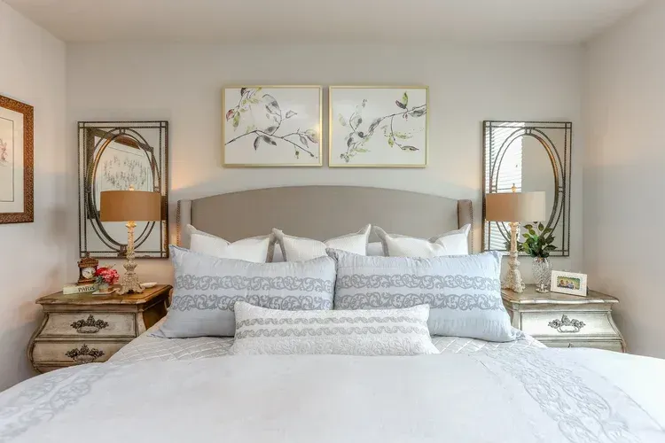 Bright bedroom with a large bed, mirrored nightstands, and floral artwork above the headboard.