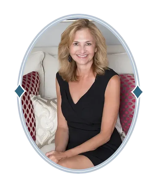 Smiling woman in a black dress seated on a couch with patterned pillows in an oval frame