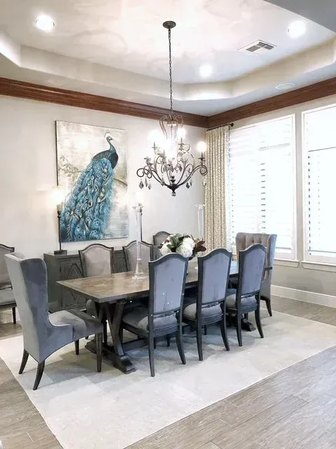 Elegant dining room with gray chairs, dark table, chandelier, peacock artwork, and large windows