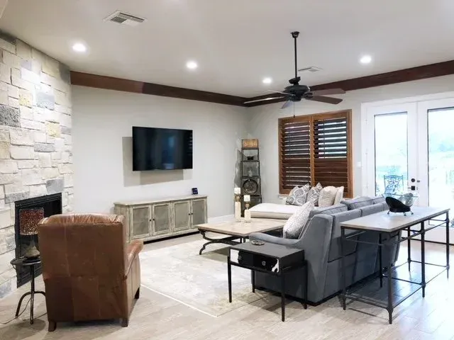 Spacious living room with stone fireplace, wall TV, gray sectional, brown chair, and glass doors to outside