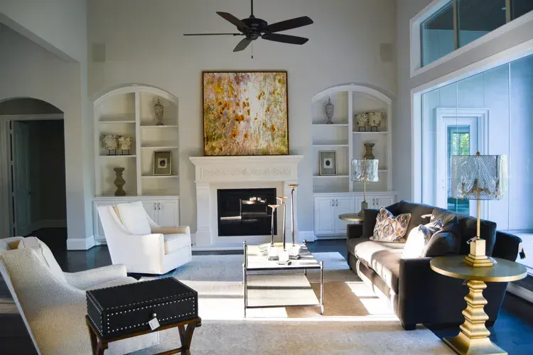 Bright living room with white walls, fireplace, black sofa, chairs, and a large abstract painting above the mantel