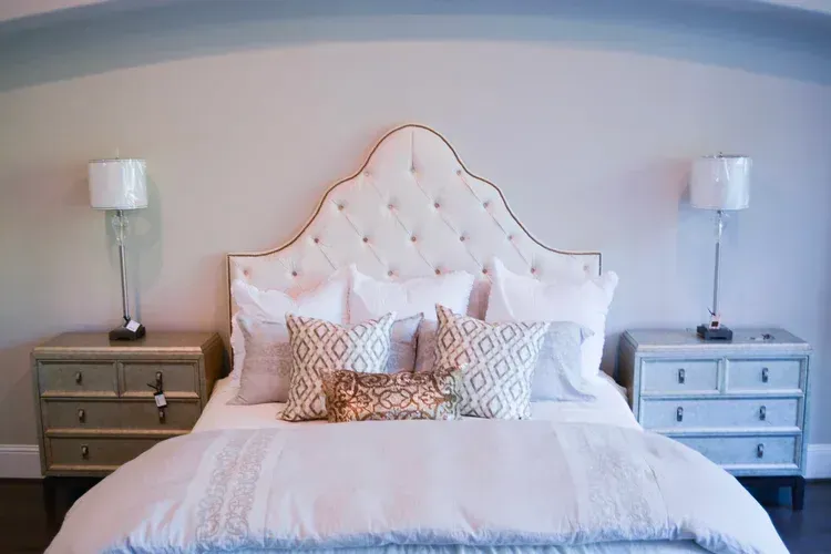 Stylish bedroom with a tufted white headboard, patterned pillows, and matching bedside tables.