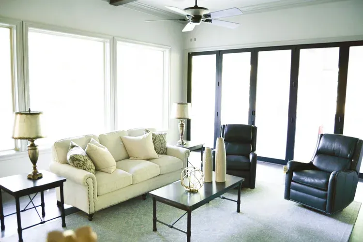 Bright living room with cream sofa, black leather chairs, glass coffee table, and large windows