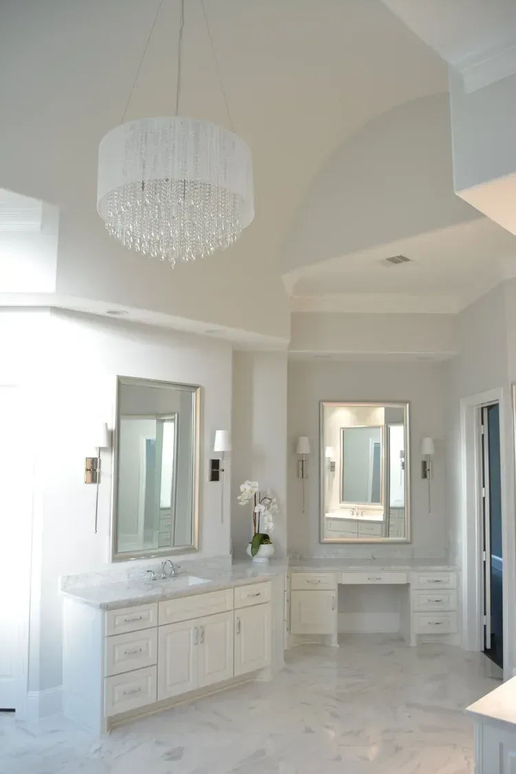 Elegant white bathroom with vanity, mirrors, chandelier, and marble floor