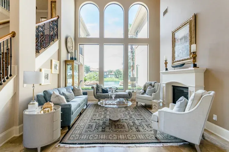 Bright living room with tall arched windows, fireplace, blue sofa, and two white armchairs