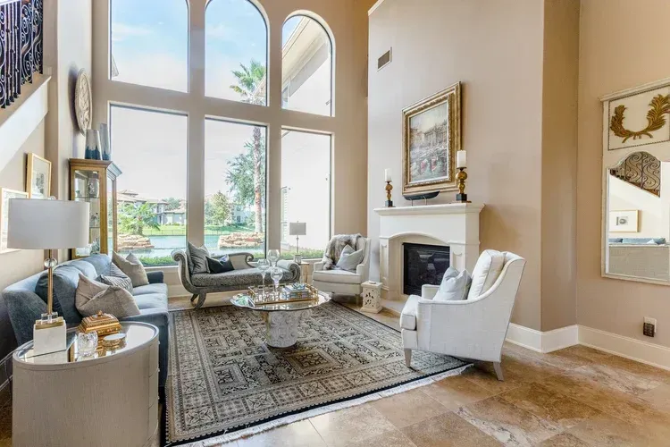Spacious living room with tall windows, fireplace, gray seating, and patterned rug