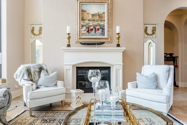 Elegant living room with white armchairs, fireplace, glass coffee table, and framed artwork