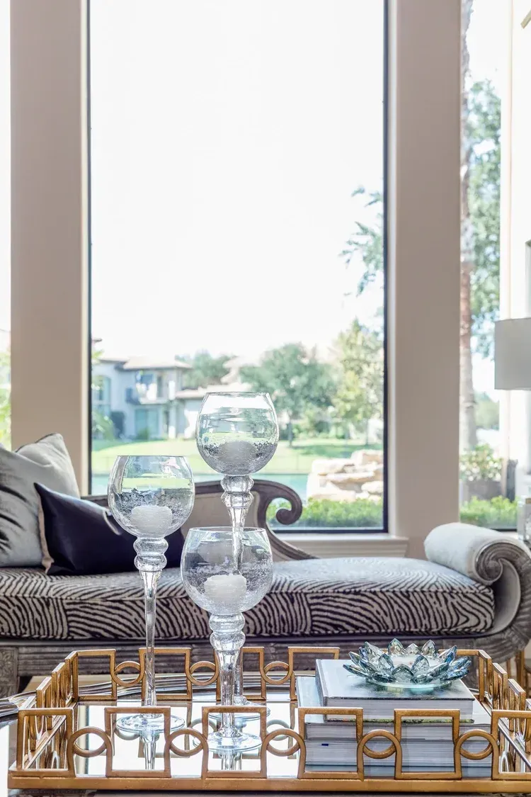Decorative glassware on a tray by a bright window, with a garden view outside.