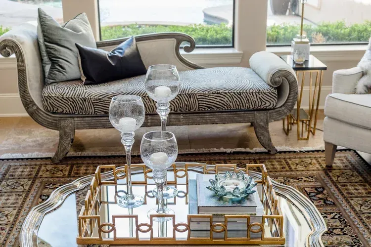 Elegant living room with a chaise lounge, glass coffee table, and patterned rug in front of bright windows